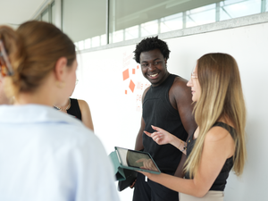 eine Studentin spricht mit 4 weiteren Studierenden. Sie hält ein iPad in ihrer Hand.