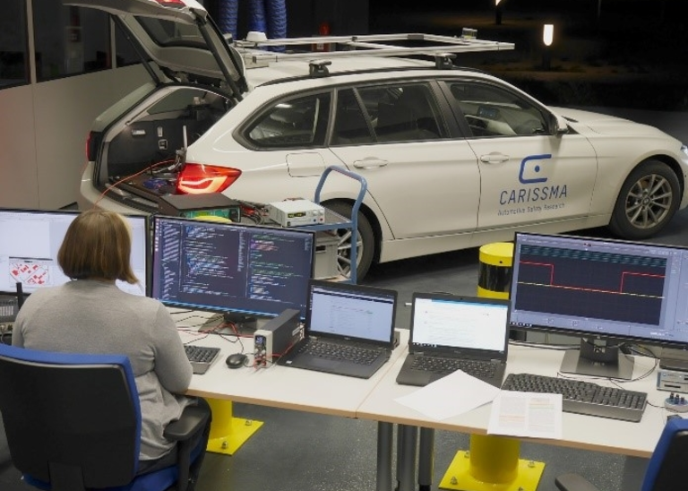 Source: THI Image of a woman sitting in front of two screens. On which system tests of applications based on Car2X communication are running