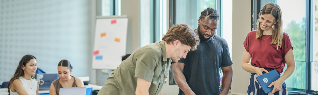 Drei Personen im Vordergrund blicken auf Laptop, hinten 2 weitere Personen