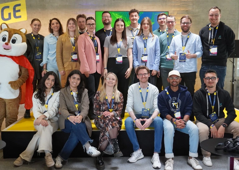 Ein Gruppenfoto mit 19 Personen und einem Maskottchen.