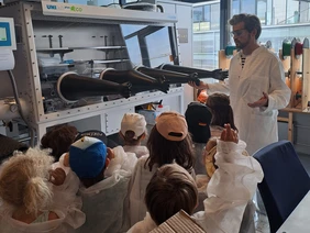 Philipp Lang welcomes the little ones at the THI (Photo: THI). Philipp Lang präsentiert den KiGa-Kindern etwas, alle mit Schutzkleidung